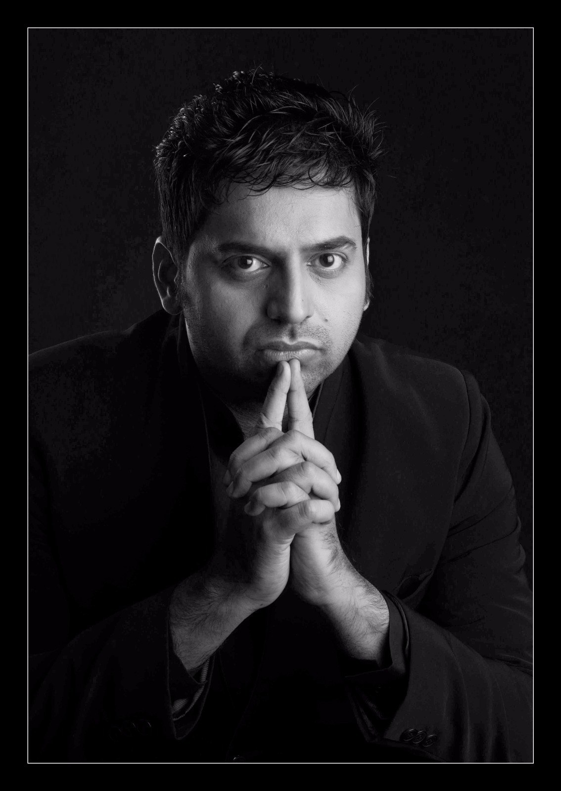 Black and white portrait of Magic Mangesh, hands clasped under his chin