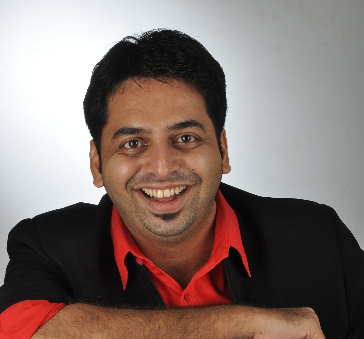 Magic Mangesh smiling, in a black jacket and red shirt
